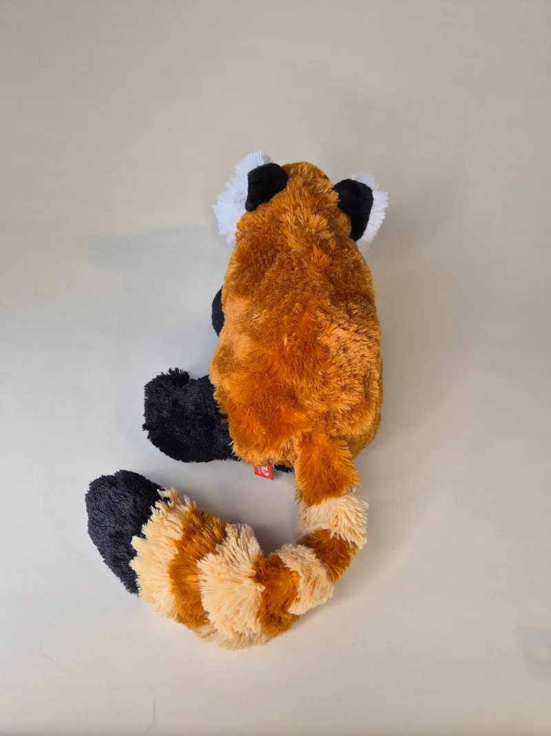 Overhead view of the red panda plush's back, with its ringed tail curved beside the body and tufted black-and-white ears visible